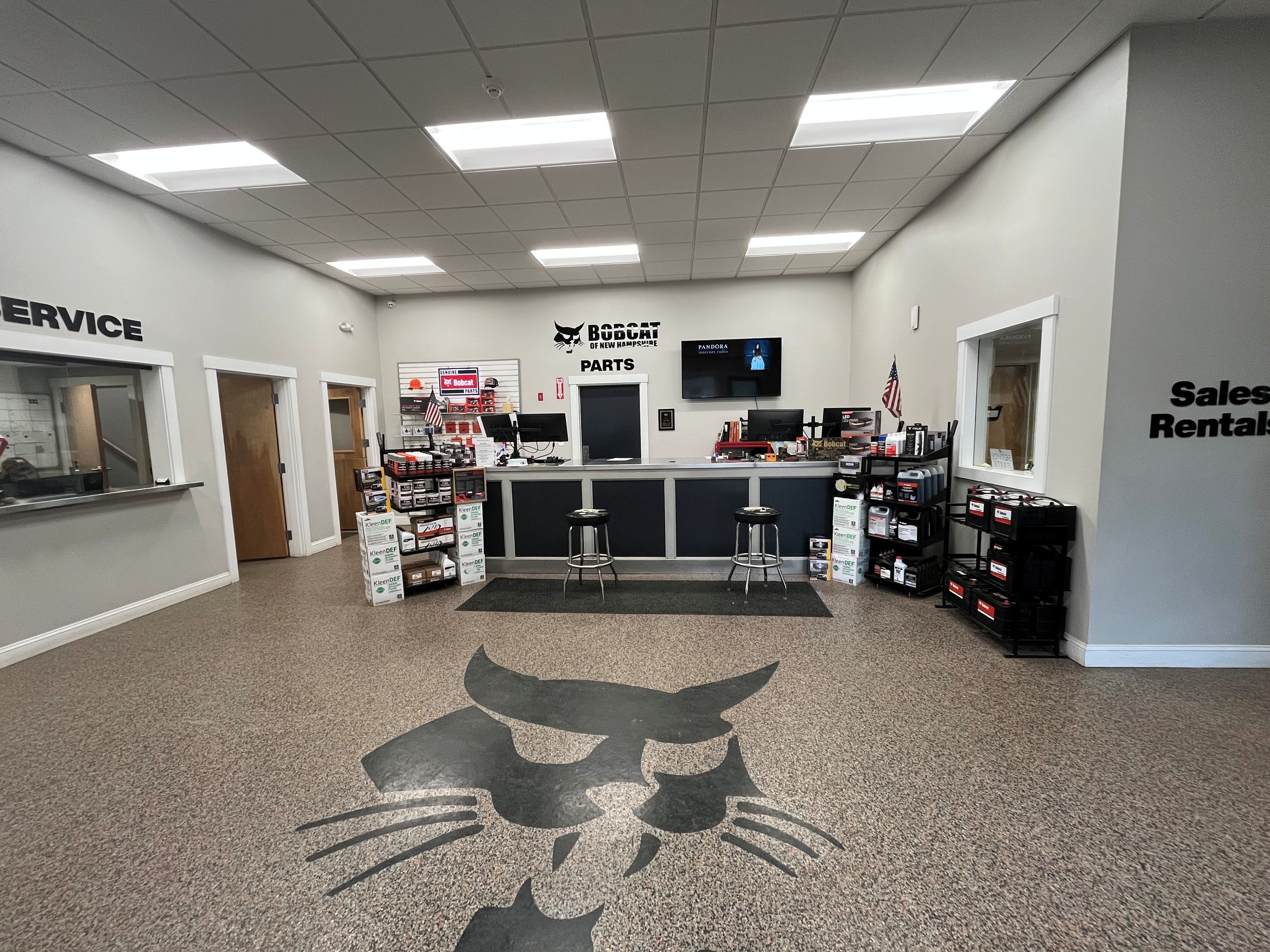 Two people working the counter at Bobcat of New Hampshire's parts department, with shelves of …